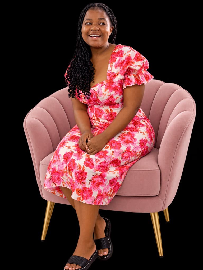 Smiling woman in a floral dress seated on a pink chair